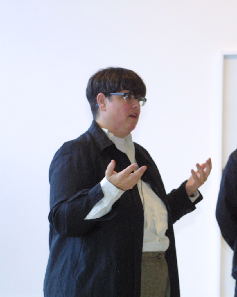 A light-skinned adult with short black hair and glasses is speaking to folks off camera.