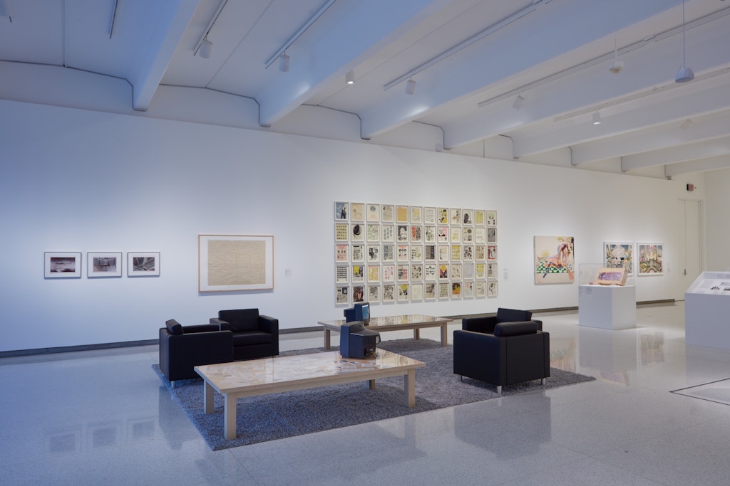 A grouping of chairs and tables sits in the middle of a gallery surrounding by several works of art.