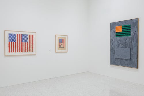 A white gallery space without any people where three paintings of American flags hang.