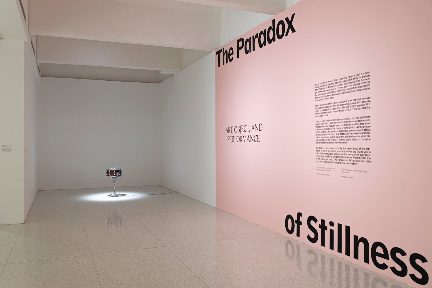 Image of pink gallery title wall with the words "The Paradox of Stillnes" and small snare drum in spotlight