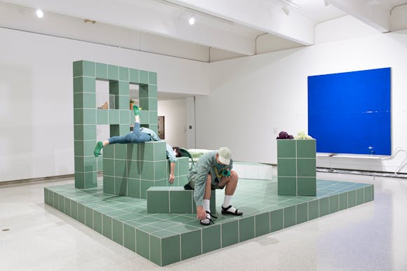 Gallery view with green block like structure and two men performing on it