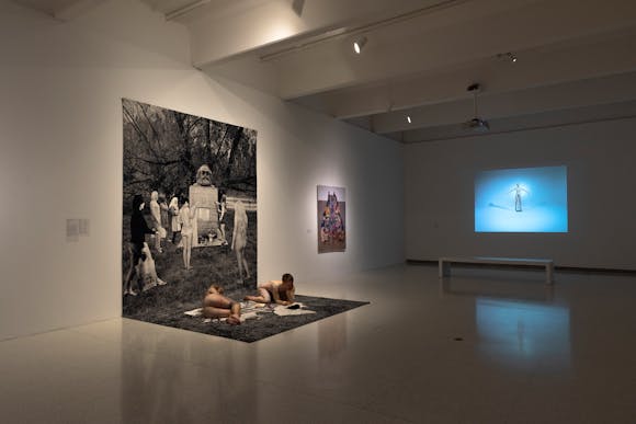 Gallery view of large print out with two performers lying on it and projection in the background