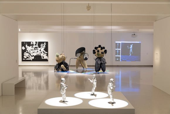 Gallery view with various sculpture objects and projections and paintings