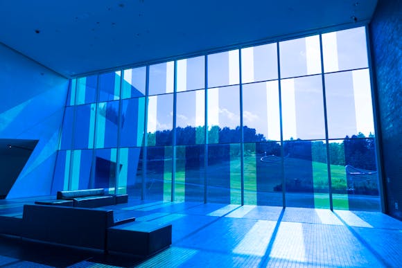 Large windows with blue checkboard decals which cast blue shadows on the floor of a lobby with couch in foreground