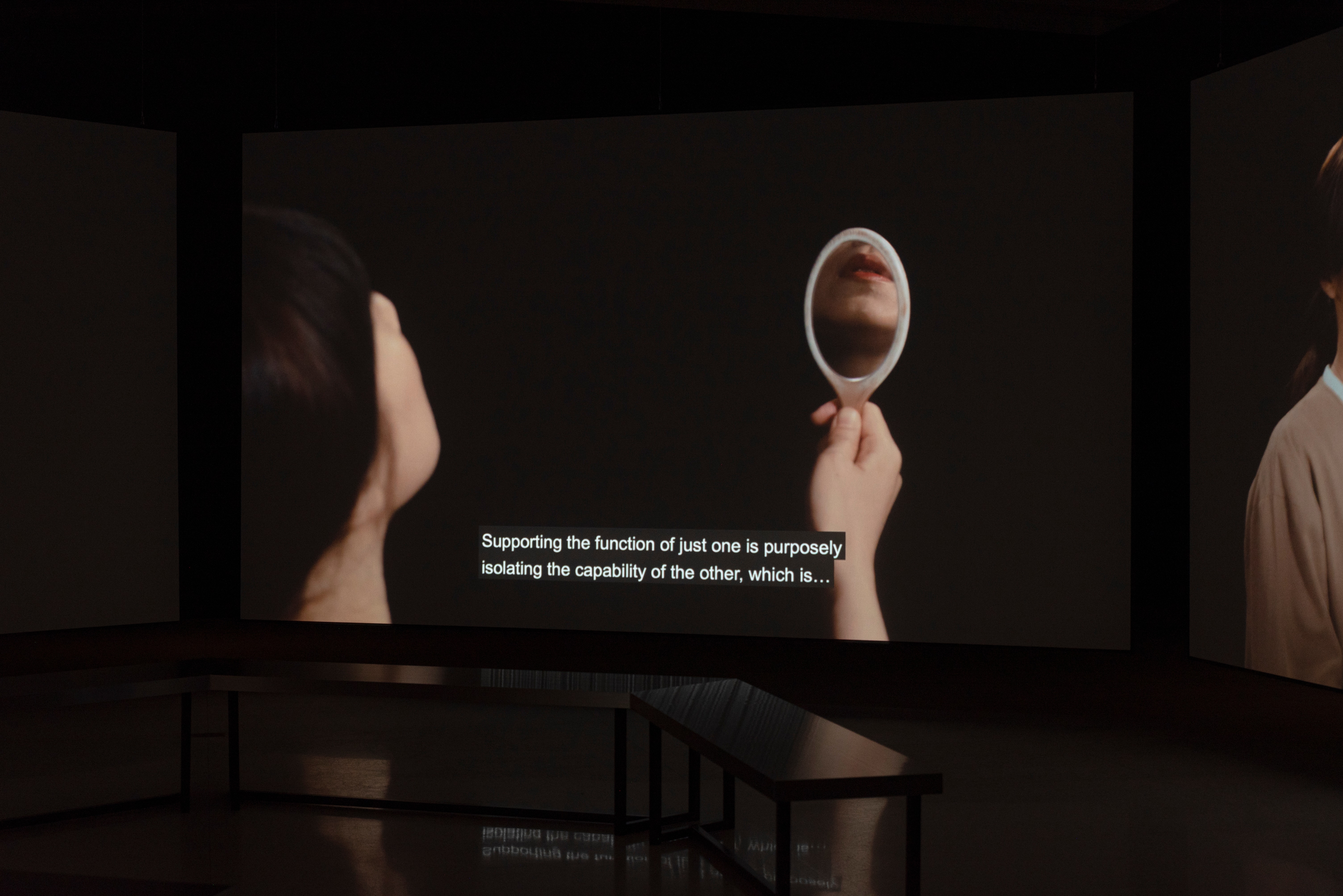 Large projection screen in dark gallery featuring image of woman holding mirror