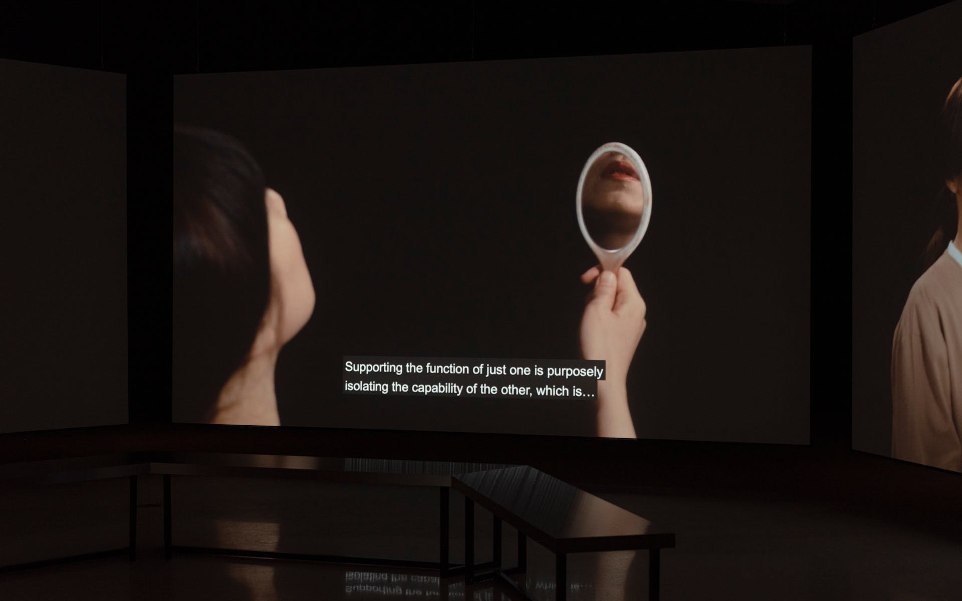 Large projection screen in dark gallery featuring image of woman holding mirror