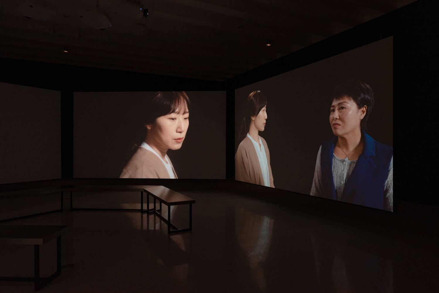 Large projection screens in dark gallery featuring images of women speaking