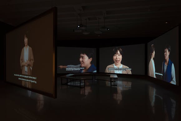 Large projection screens in dark gallery featuring images of women speaking