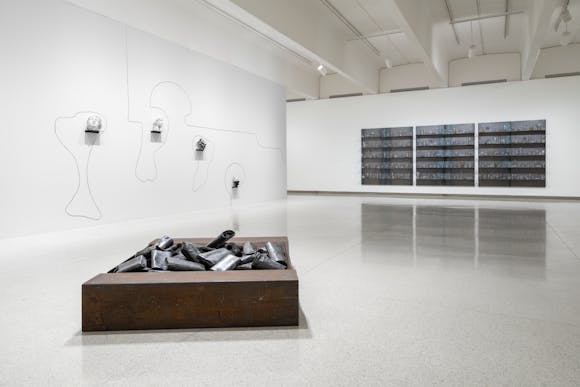 A sculpture sist on the floor and two hang from walls in an art gallery.