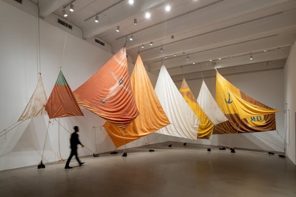 A person walks past a sculpture of several large sails in an art gallery.