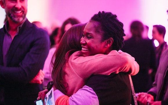 Two adults smile and hug in a crowd bathed in colored lights in a museum lounge.