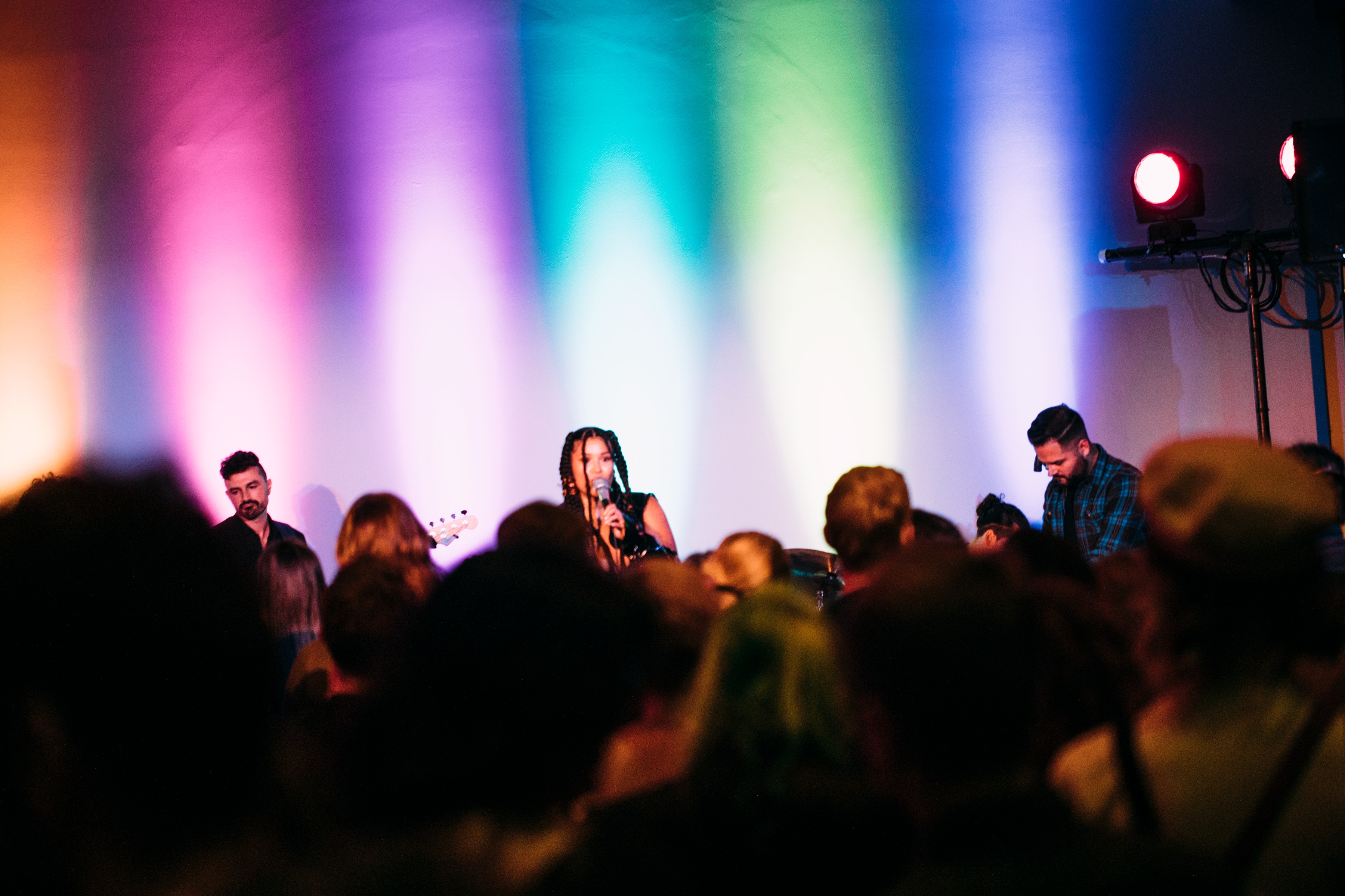 A band plauys on a stage in front of colored lights as a group dances in front of them.