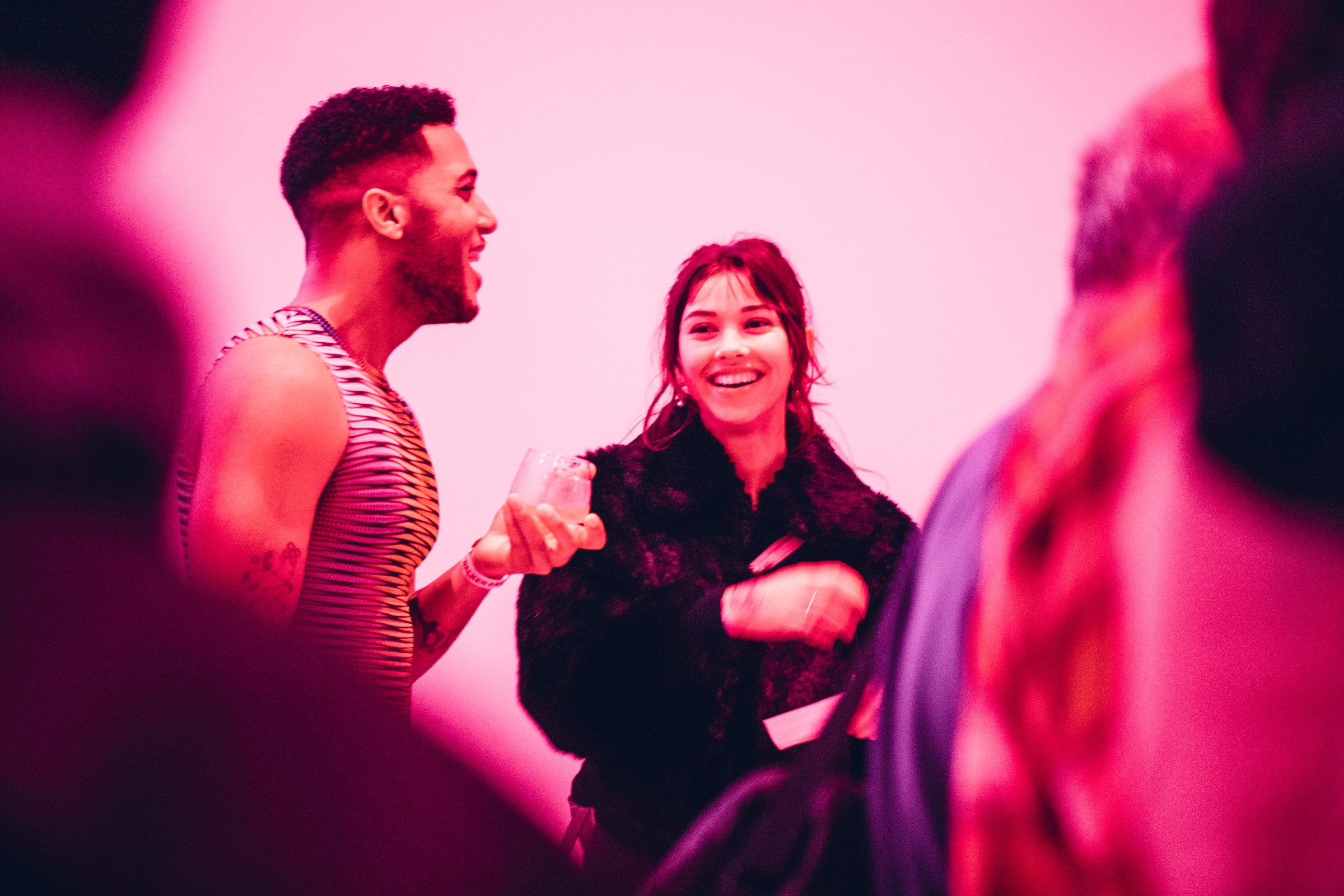 Two adults laughing in a gallery space that is lit pink