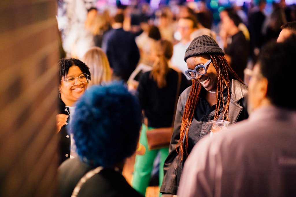 A group of people smiling and talking at a lively indoor social event.
