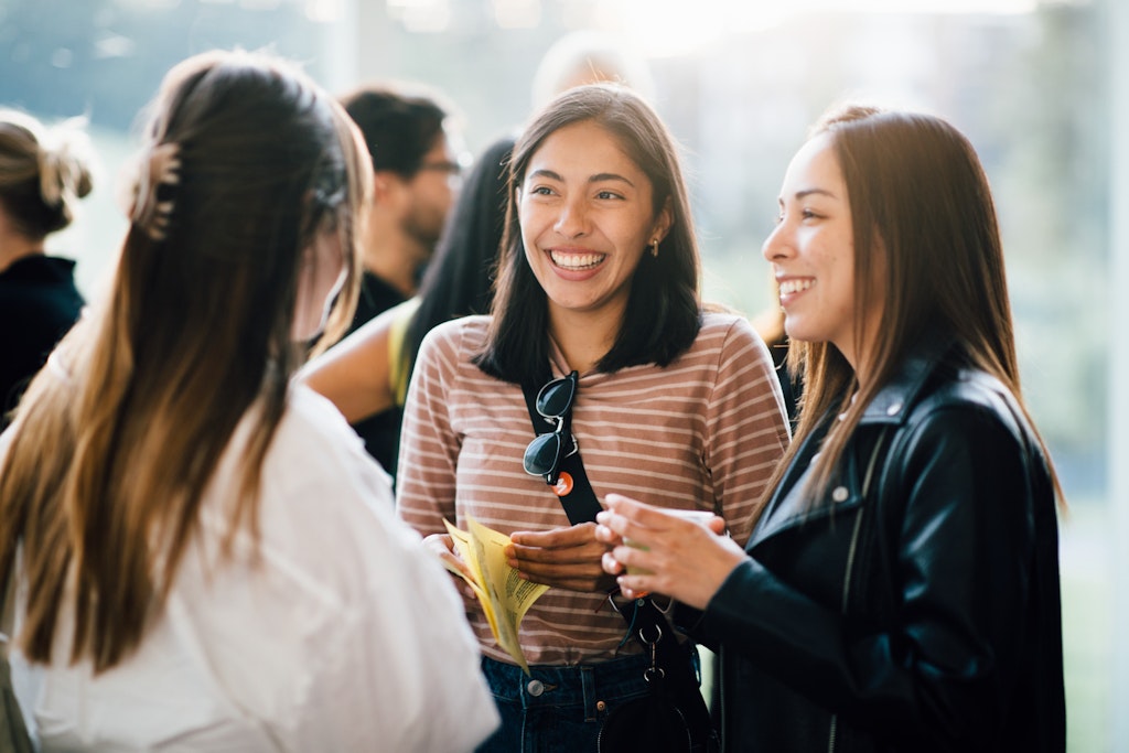 Three young women smile and chat together at an indoor social gathering or event.