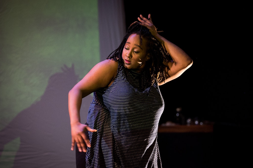 A woman moves her body in front of a projection in a dark room.