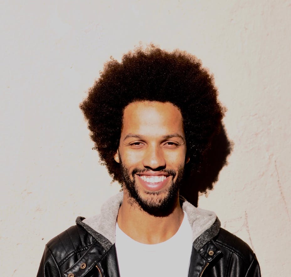 A person with medium dark skin and medium long hair smiles while looking forward.