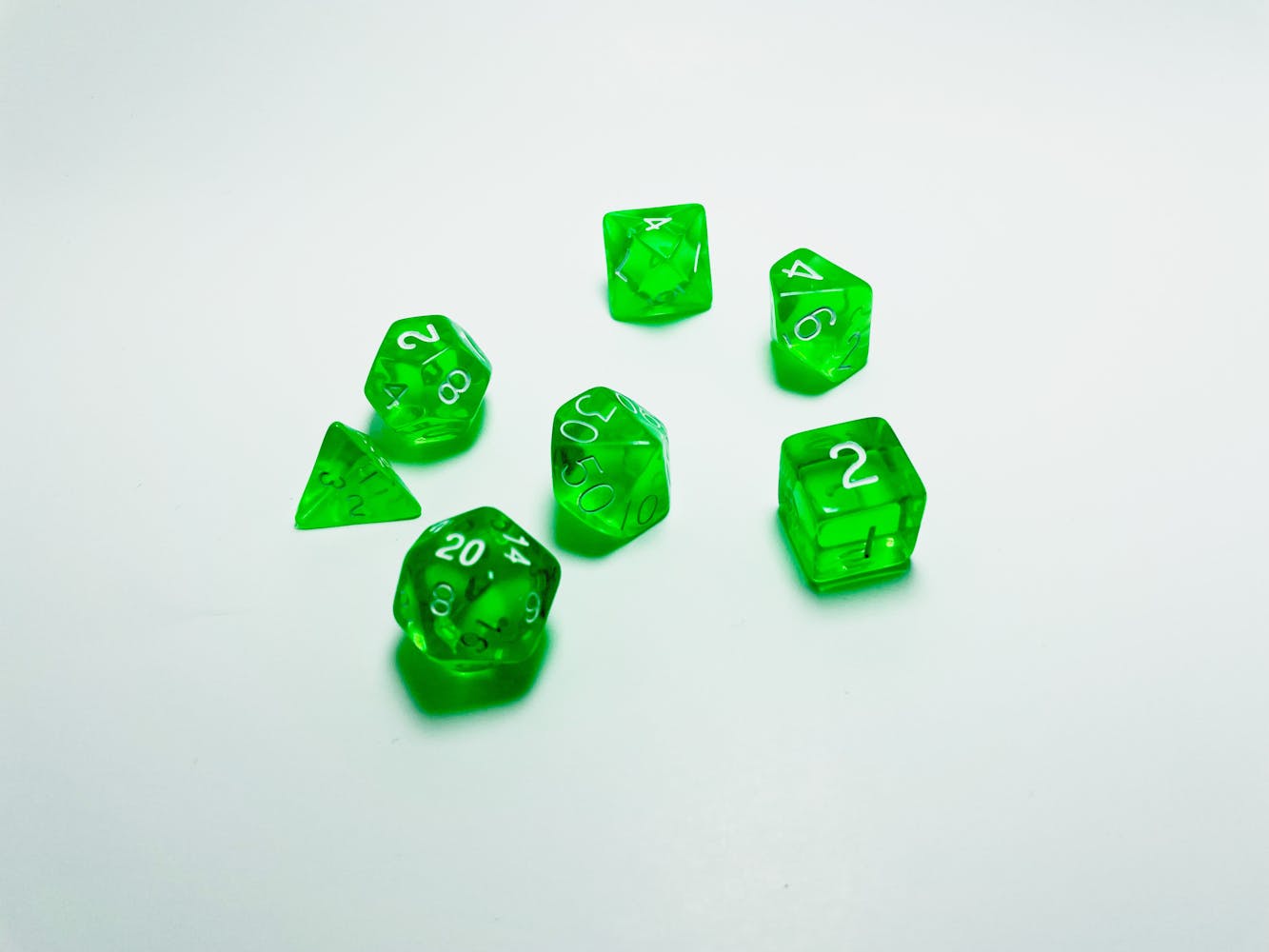 A group of green role playing dice lay on a white counter.