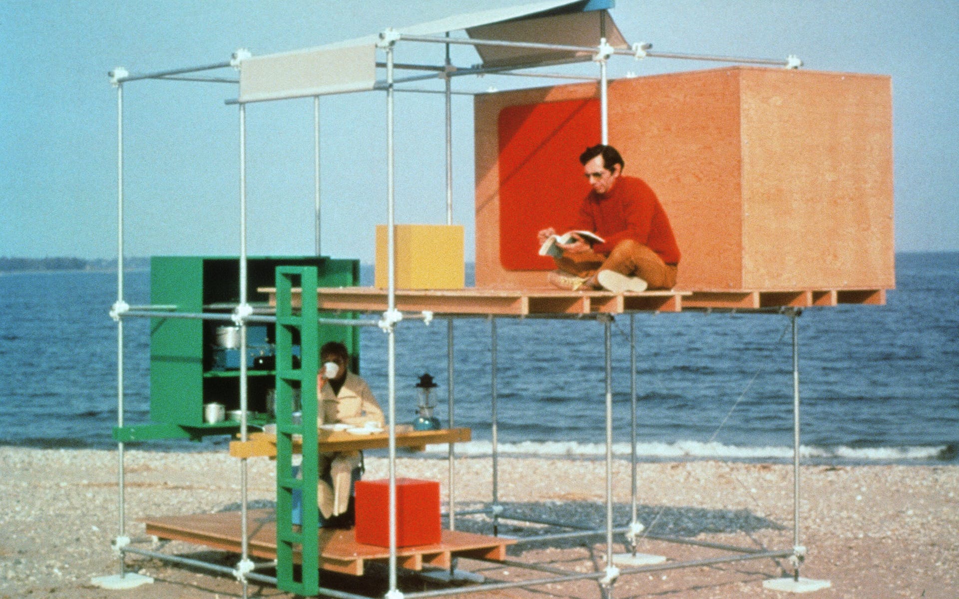 Two men sitting in a two-story structure made of metal poles and wooden panels on the beach