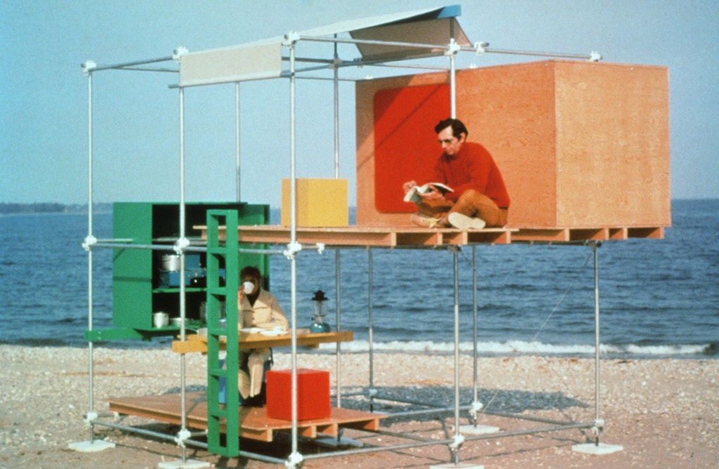 Two men sitting in a two-story structure made of metal poles and wooden panels on the beach