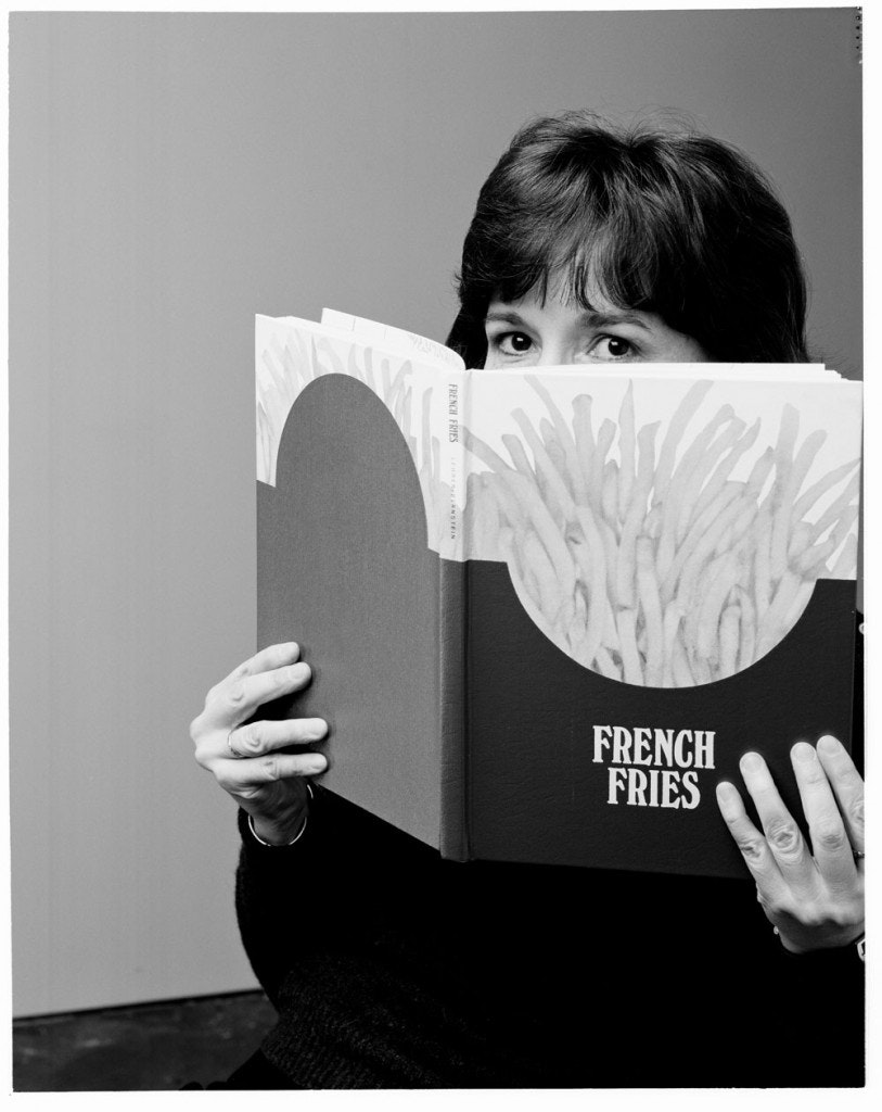 A woman cover the bottom half of her face with a book that looks like a McDonalds french fry box.