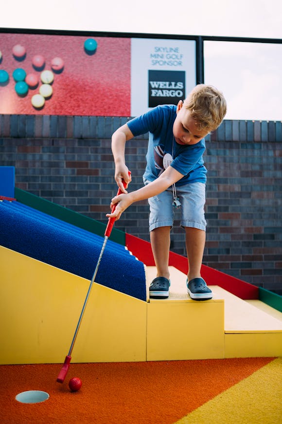 young boy about to put ball on multicolor minigolf course
