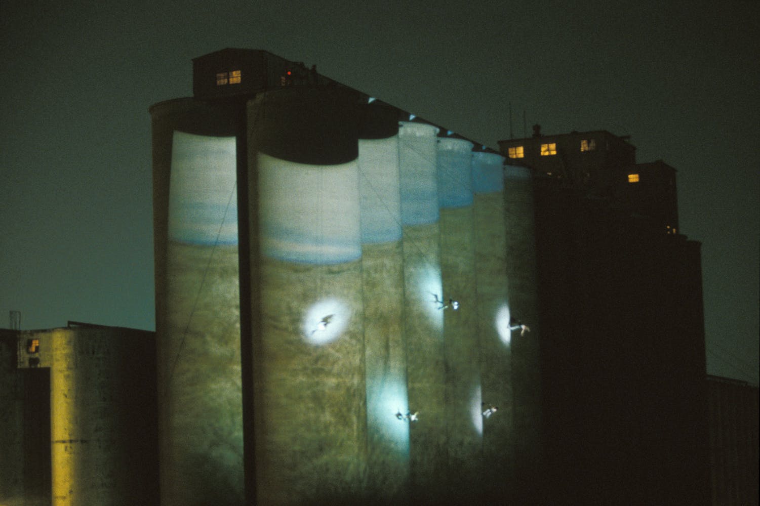 Dancers suspended from the top of a large grain silo dance on its exterior with projections.