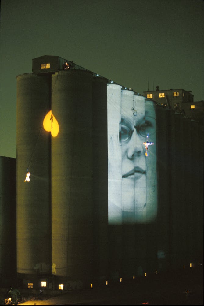 Dancers suspended from the top of a large grain silo dance on its exterior with projections.