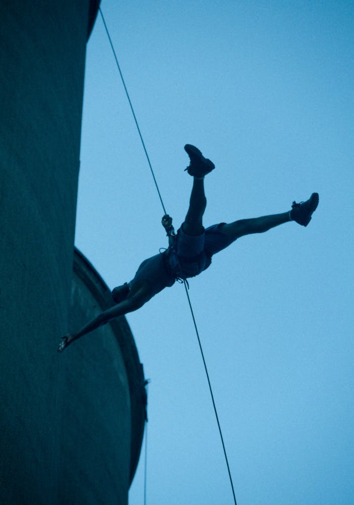 Dancers suspended from the top of a large grain silo dance on its exterior with projections.