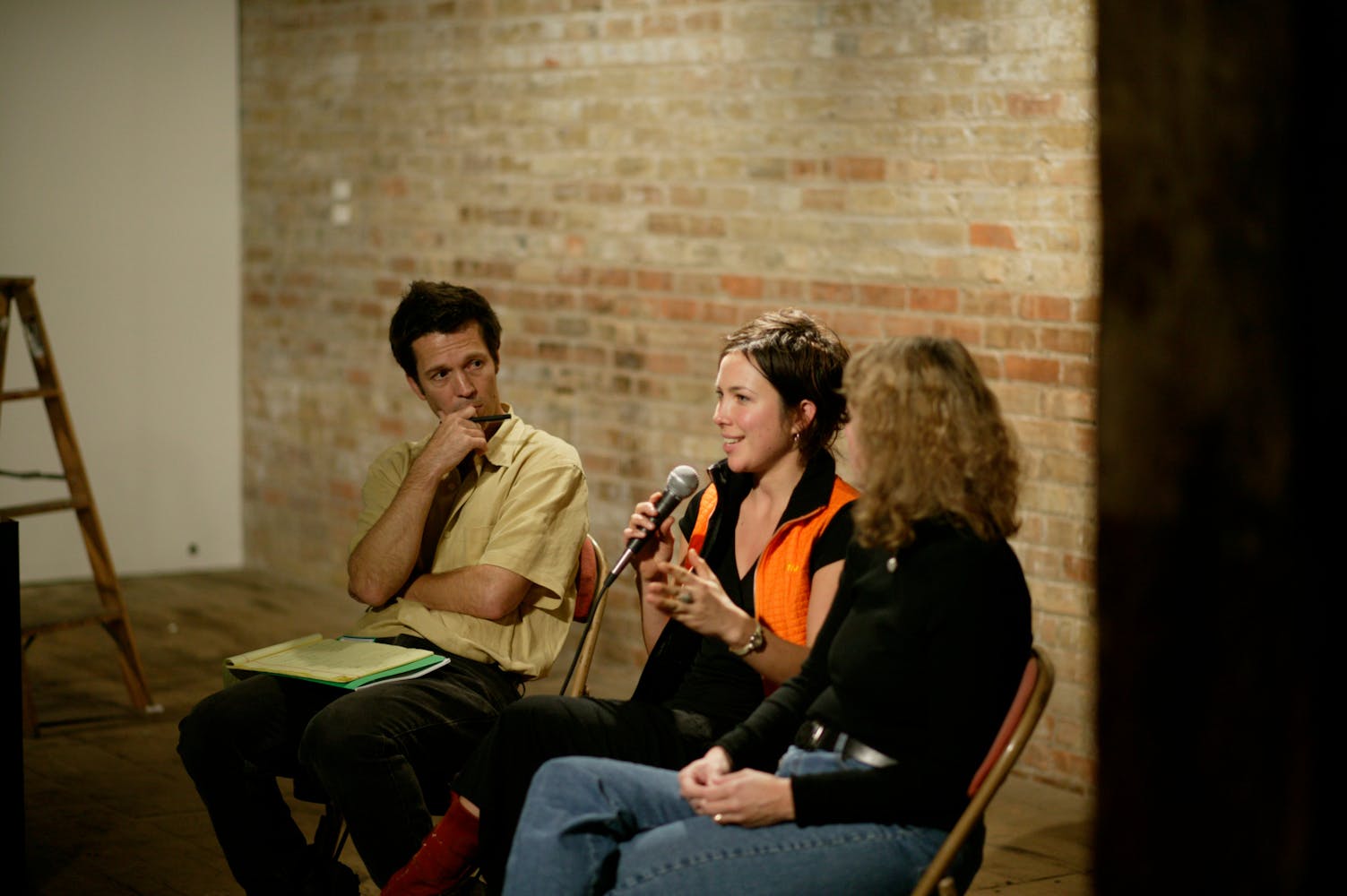 Three adults sit in charis while speaking into a microphone.