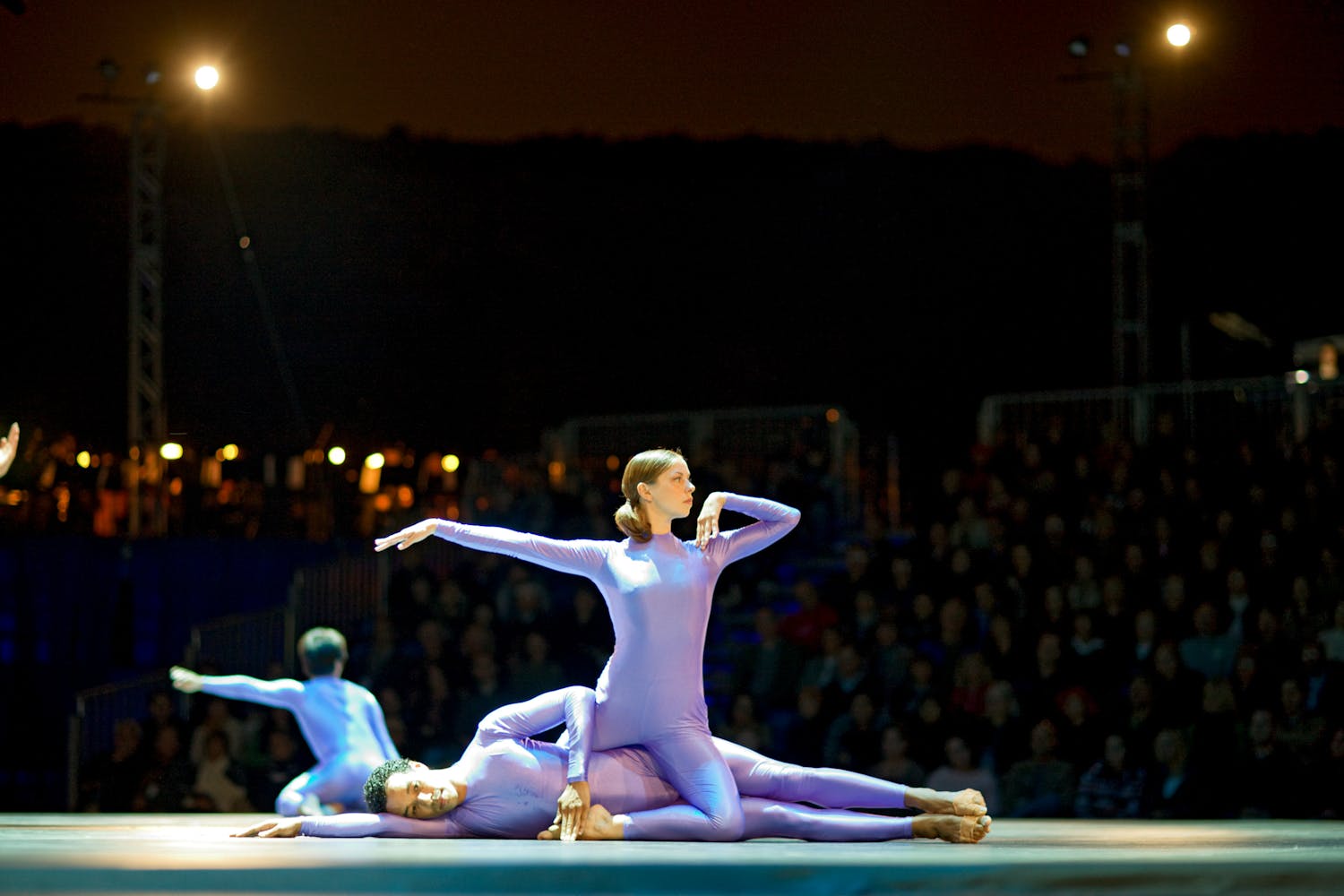 Dancers perform on a large stage in aquarry at night.