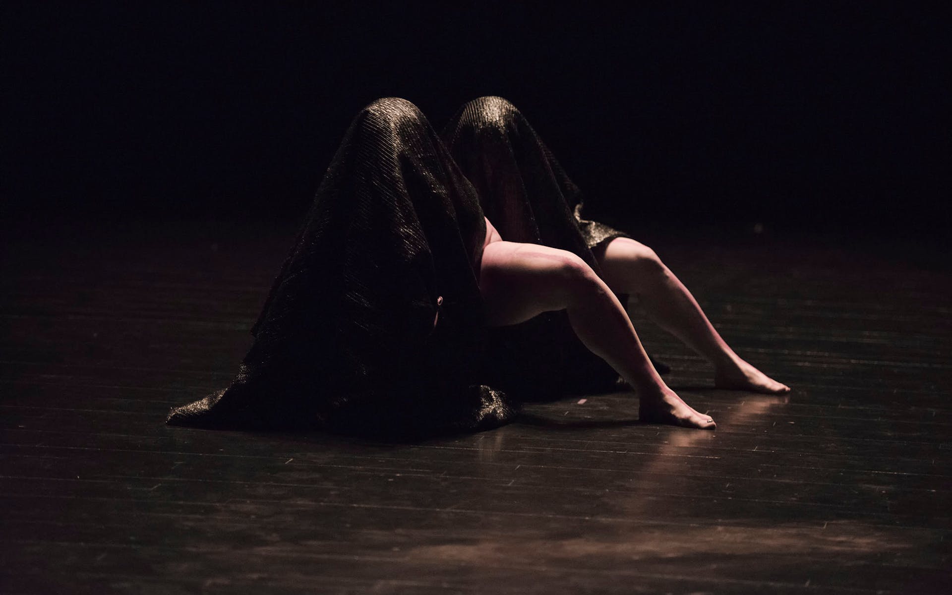 Dancers cloaked in dark fabric.
