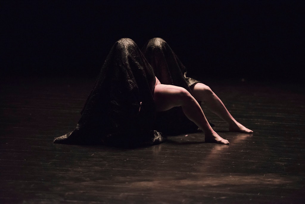 Dancers cloaked in dark fabric.
