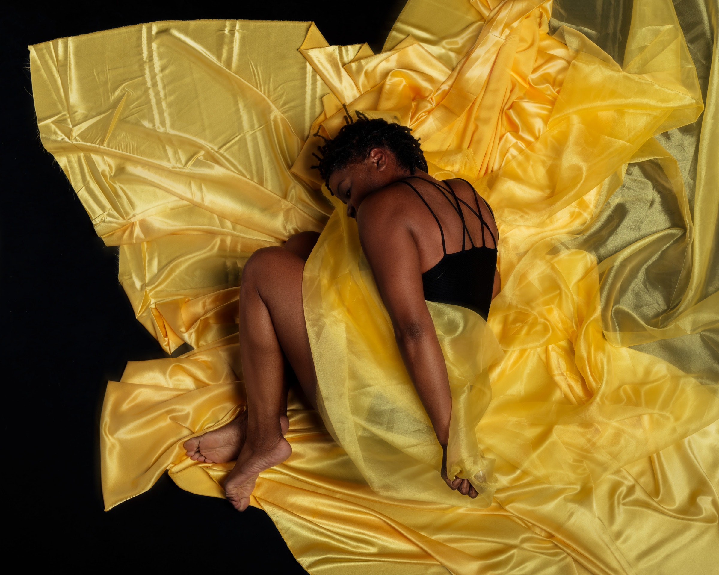 A woman lies curled up in lots of sheer yellow fabirc.