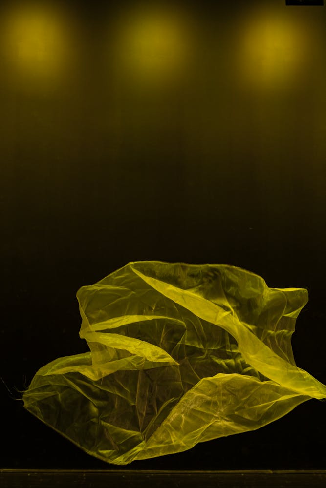 A sheer yellow piece of fabirc sloats in the air on an empty, black stage.