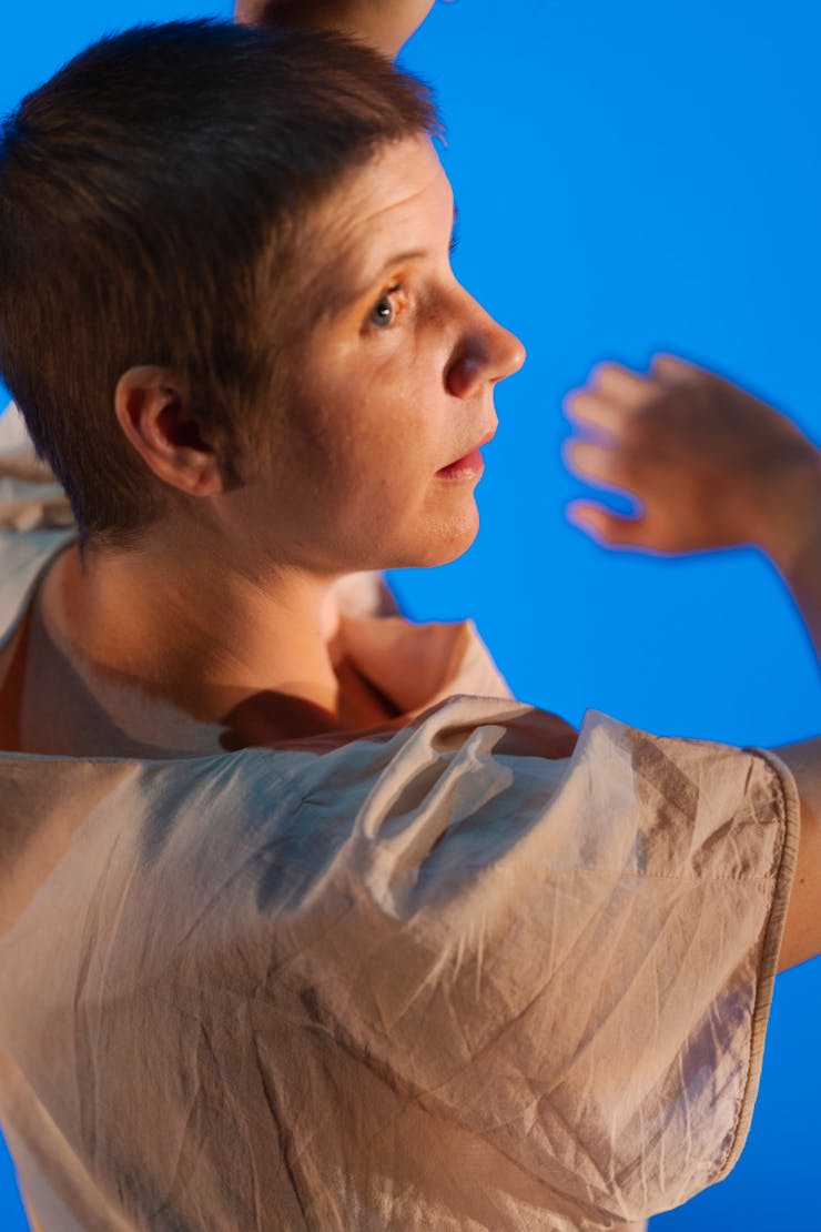 Dancer wearing beige and looking over shoulder in front of a blue background