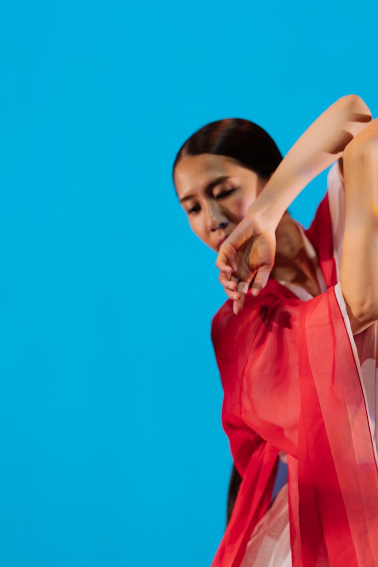 Dancer in the right of the frame looking down behind their raised arm in front of a blue background