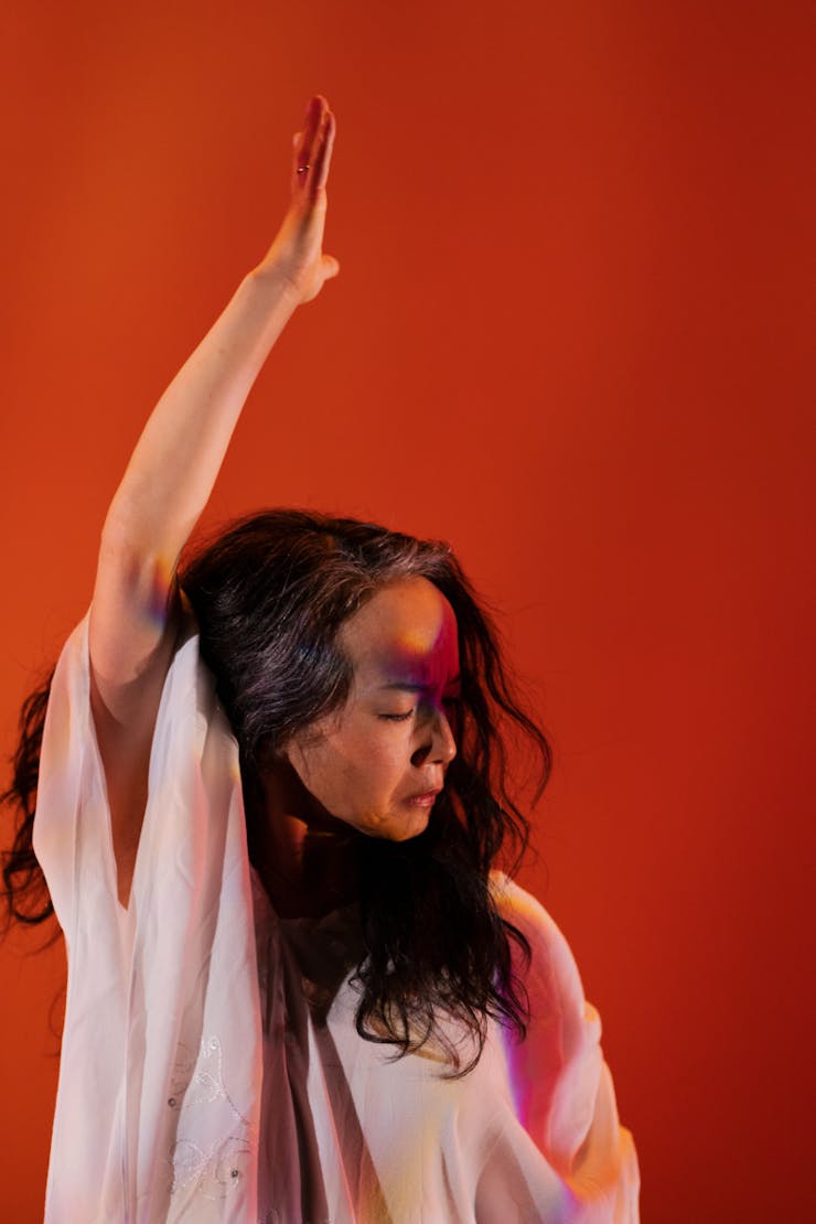 Dancer with eyes closed lifting right hand up in front of a red background