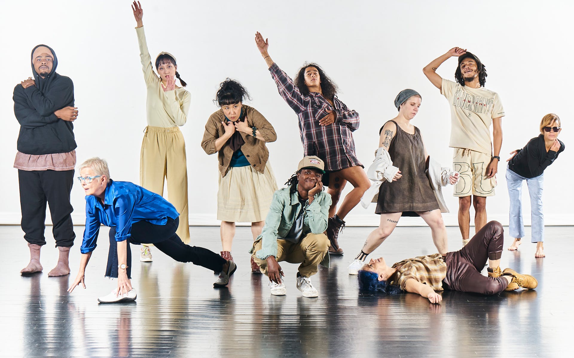 A group of dancers pose on a stage with a white background.