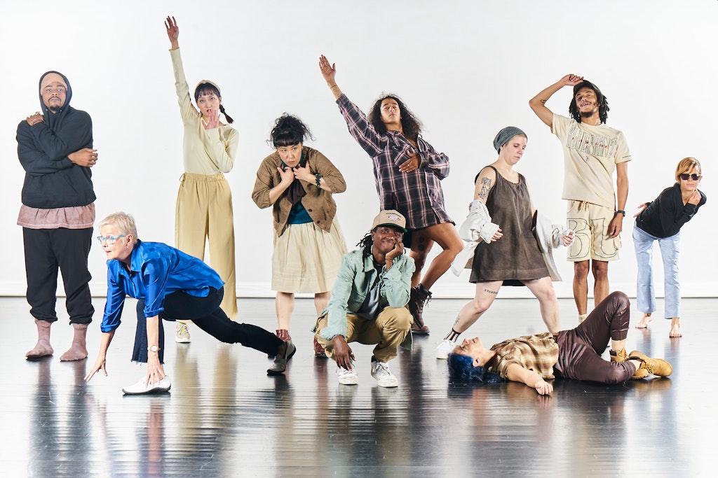 A group of dancers pose on a stage with a white background.