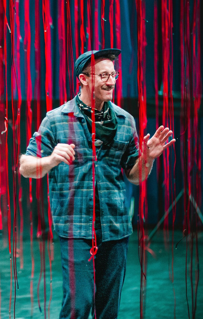 A man stands with a smile on his face amongst hanging red strips.