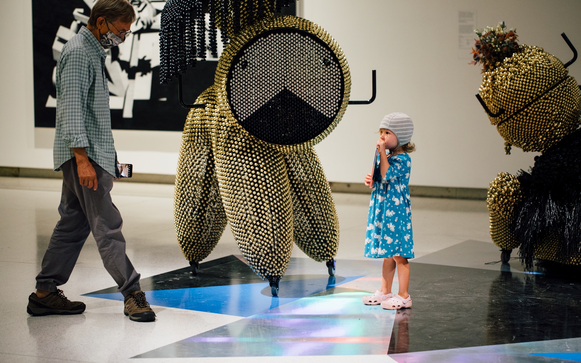 A child stands in a gallery with sculptures by an adult.