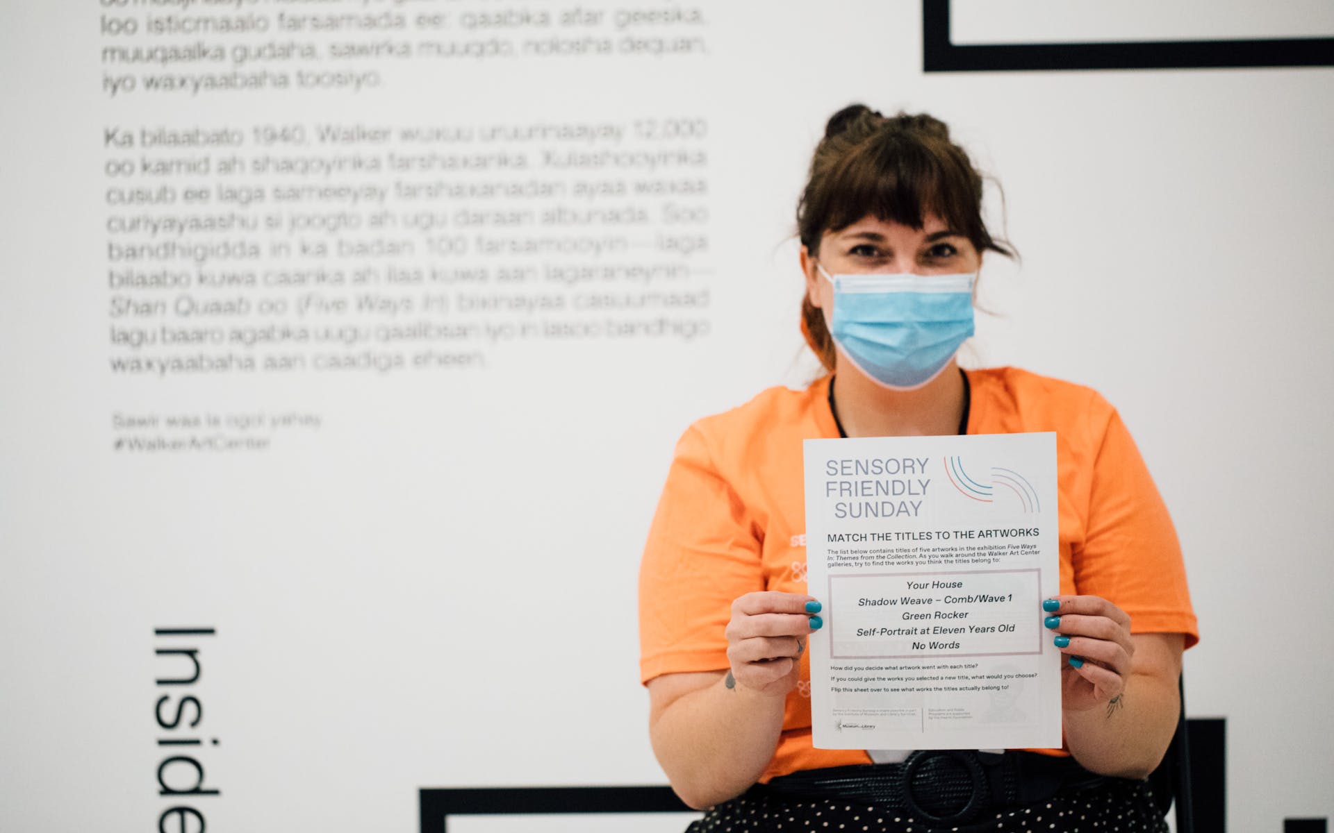 An adult wearing a face mask holds up a sheet with instructions at the viewer.