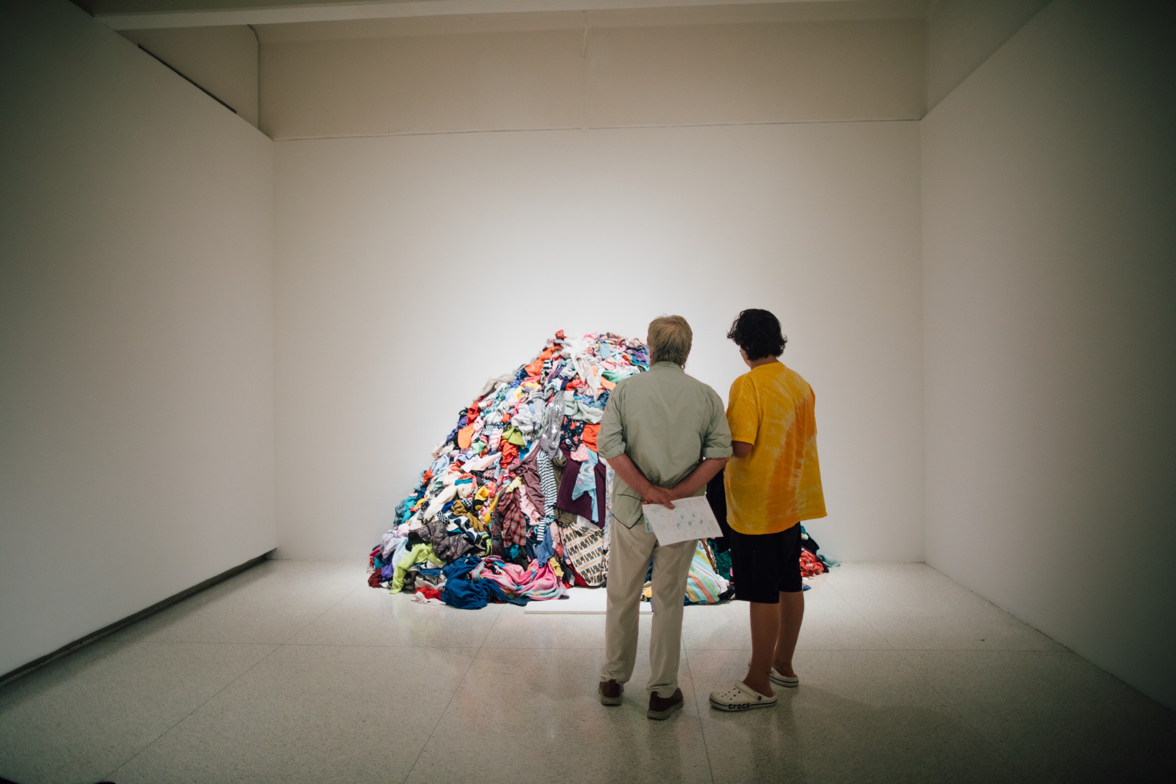 Two adults look at a pile of clothing in a white museum gallery.