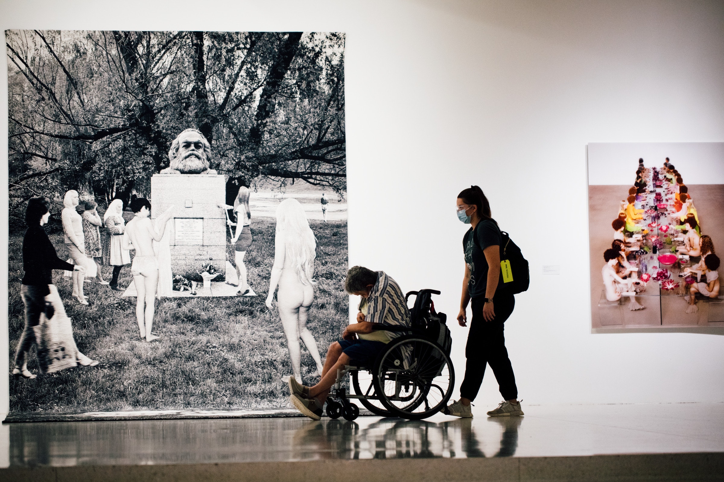 Two adults, one standing and one in a wheelchair, stand in a gallery space in front of art.