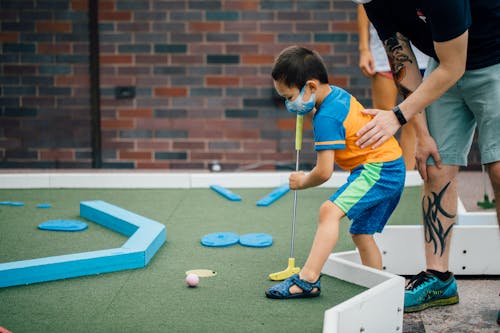 An adult helps a child play mini golf.