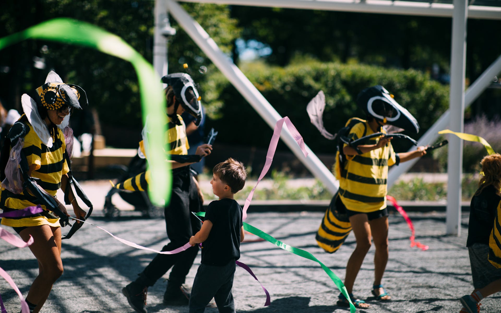 A child dances with two adults in bee costumes among streamers outside.