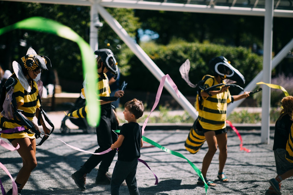A child dances with two adults in bee costumes among streamers outside.