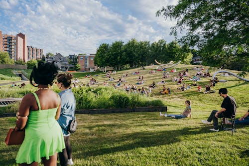 A crowd of people lay on blankets on a scultpure garden hillside and listen to a live poetry reading.