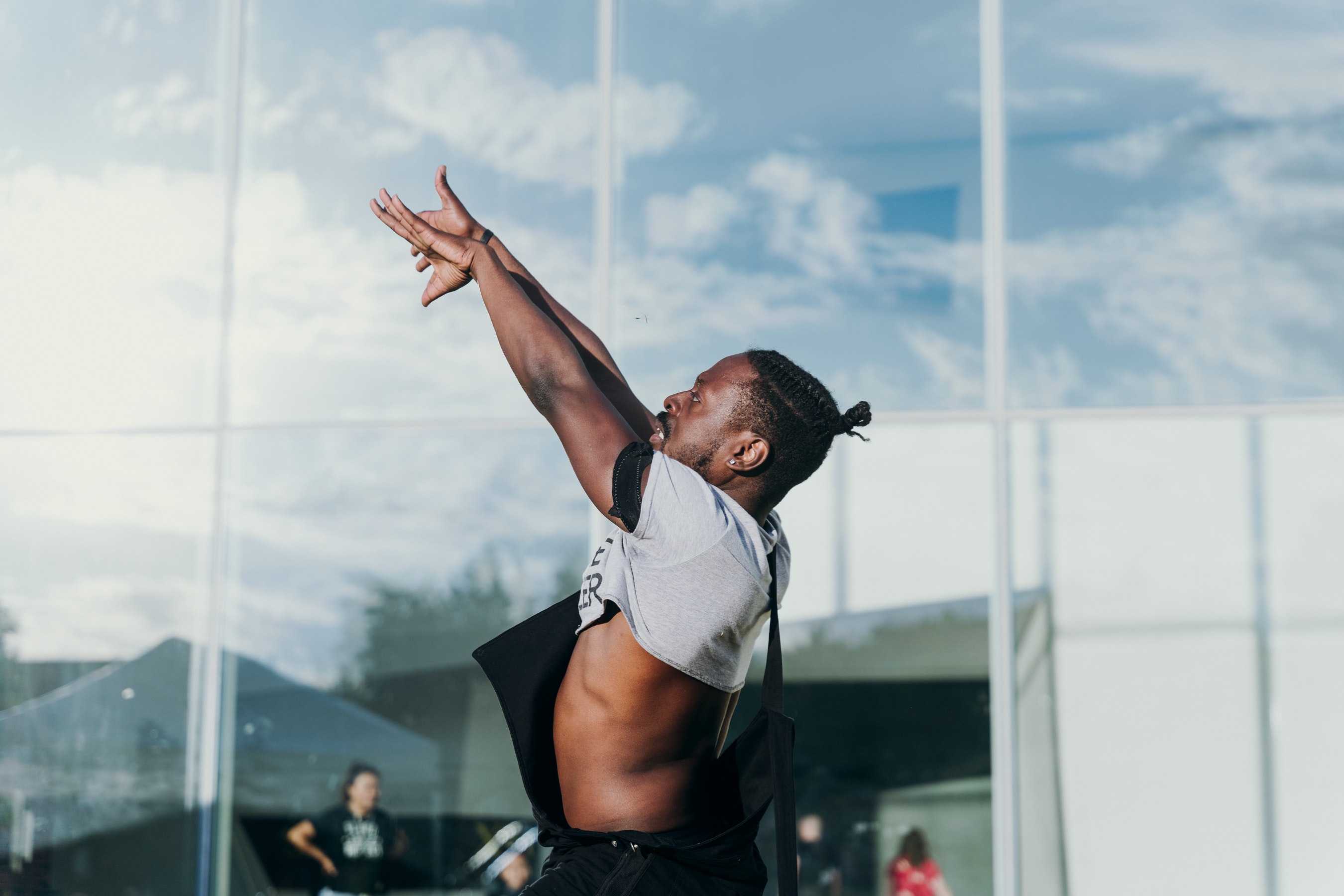 An adult folds their arms out in frnt of them as they dance outside of a museum on a sunny summer day.
